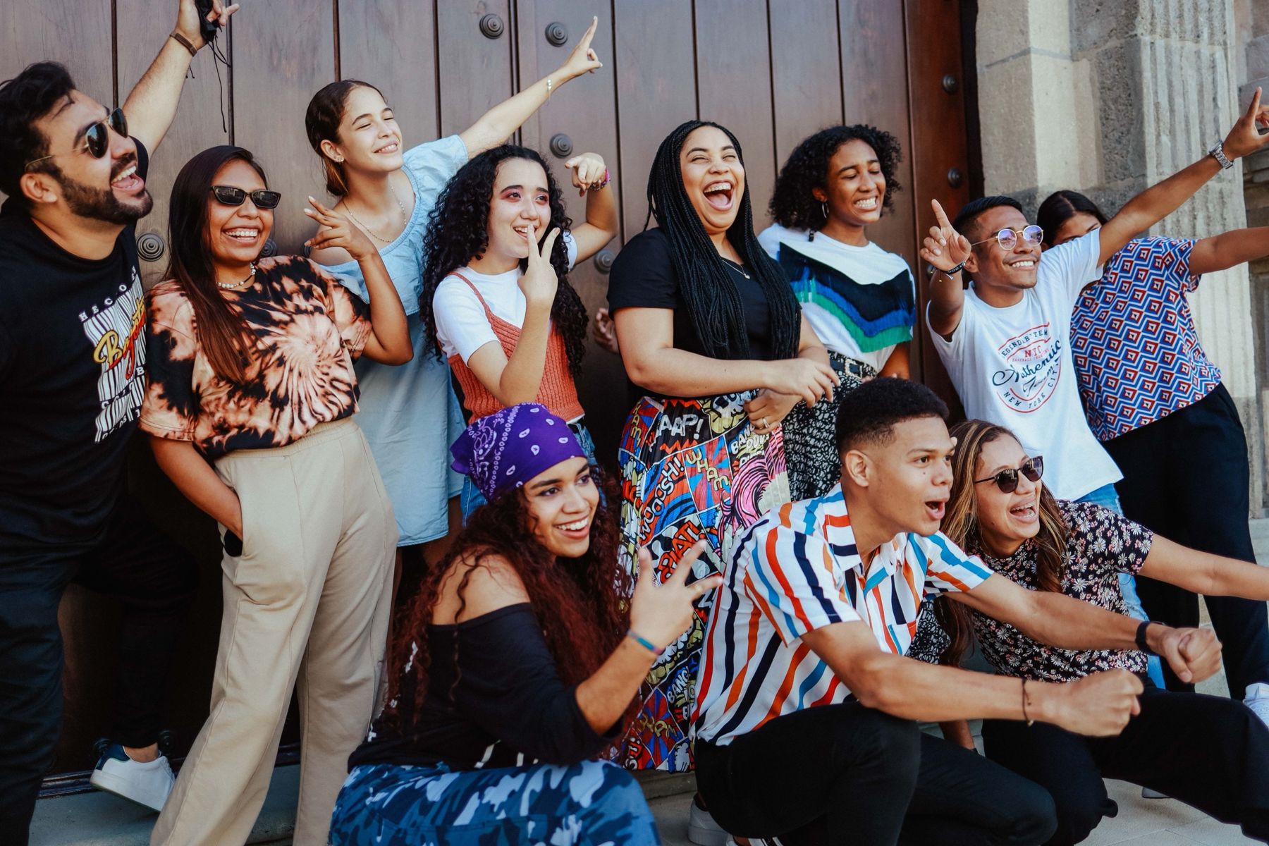 A group of young people from different backgrounds laughing together in front of a historic wooden door